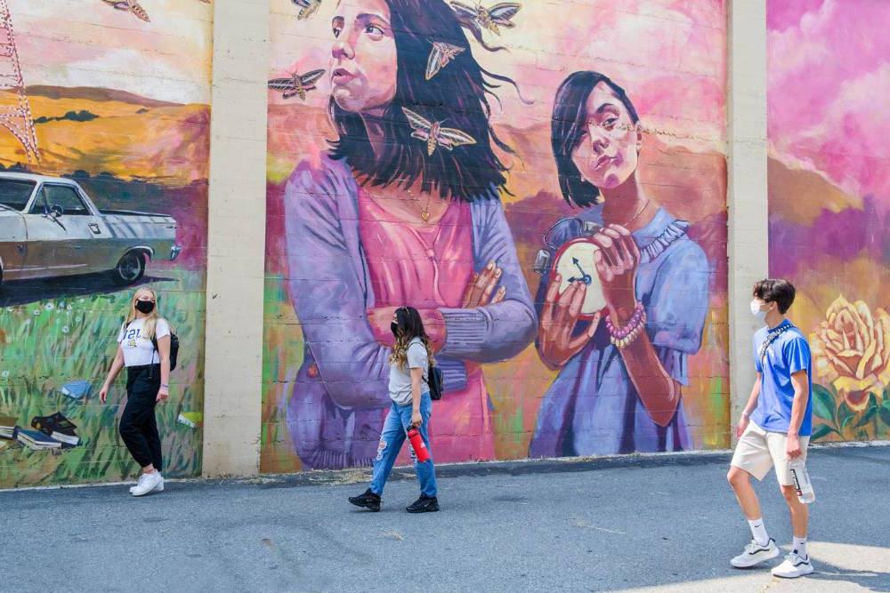 学生 roaming downtown in front of a colorful mural.